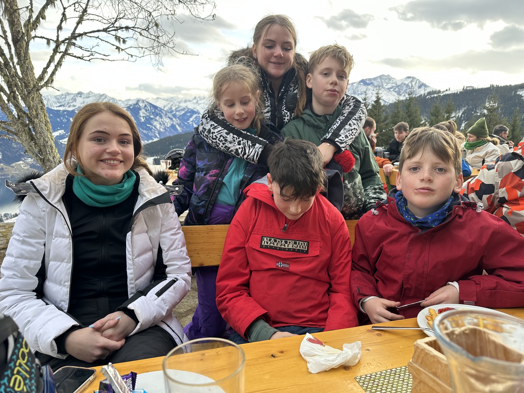 A group gathered around an outdoor table with snowy mountains behind them.