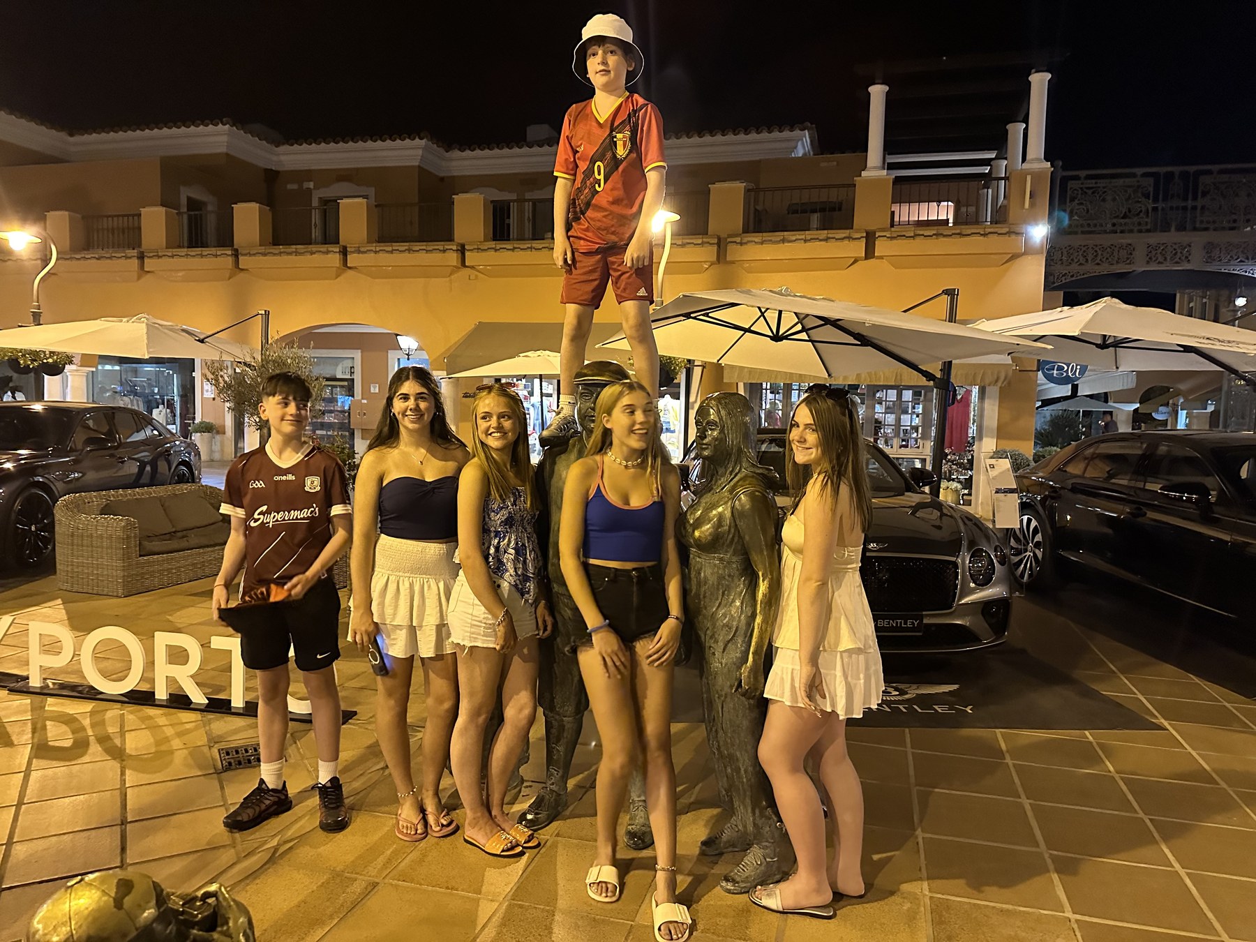 A group posing beside a statue in a brightly lit square at night.