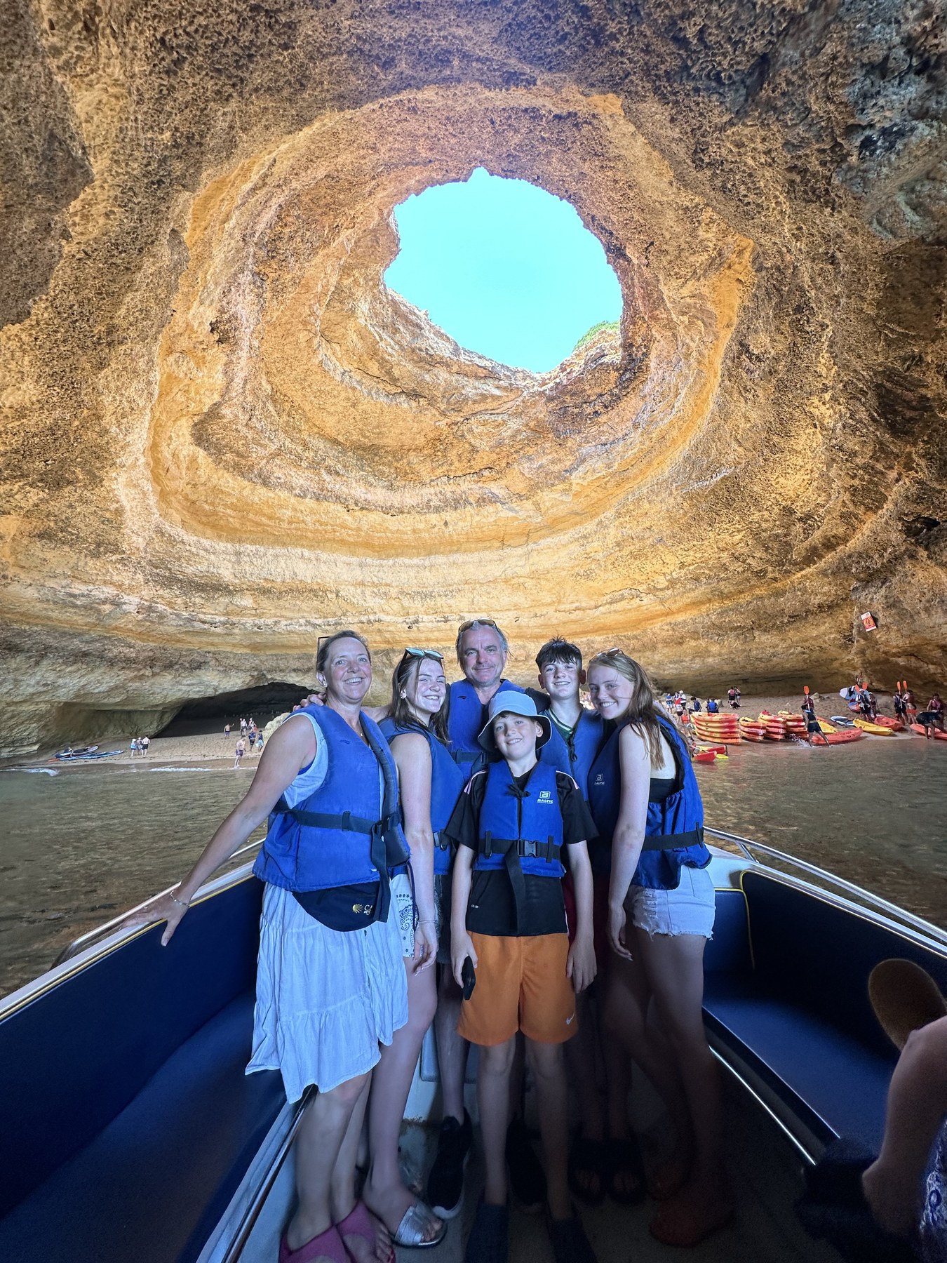 A group wearing lifejackets on a boat inside a sunlit sea cave.