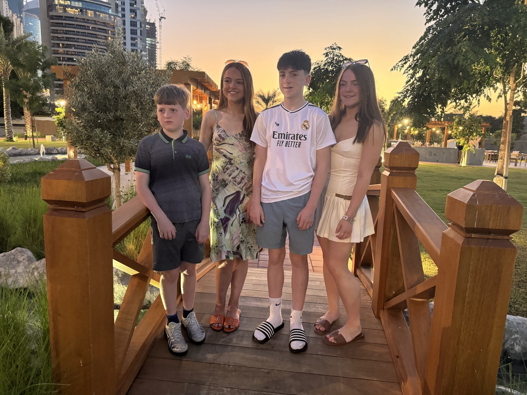 Four people standing on a wooden footbridge at sunset.