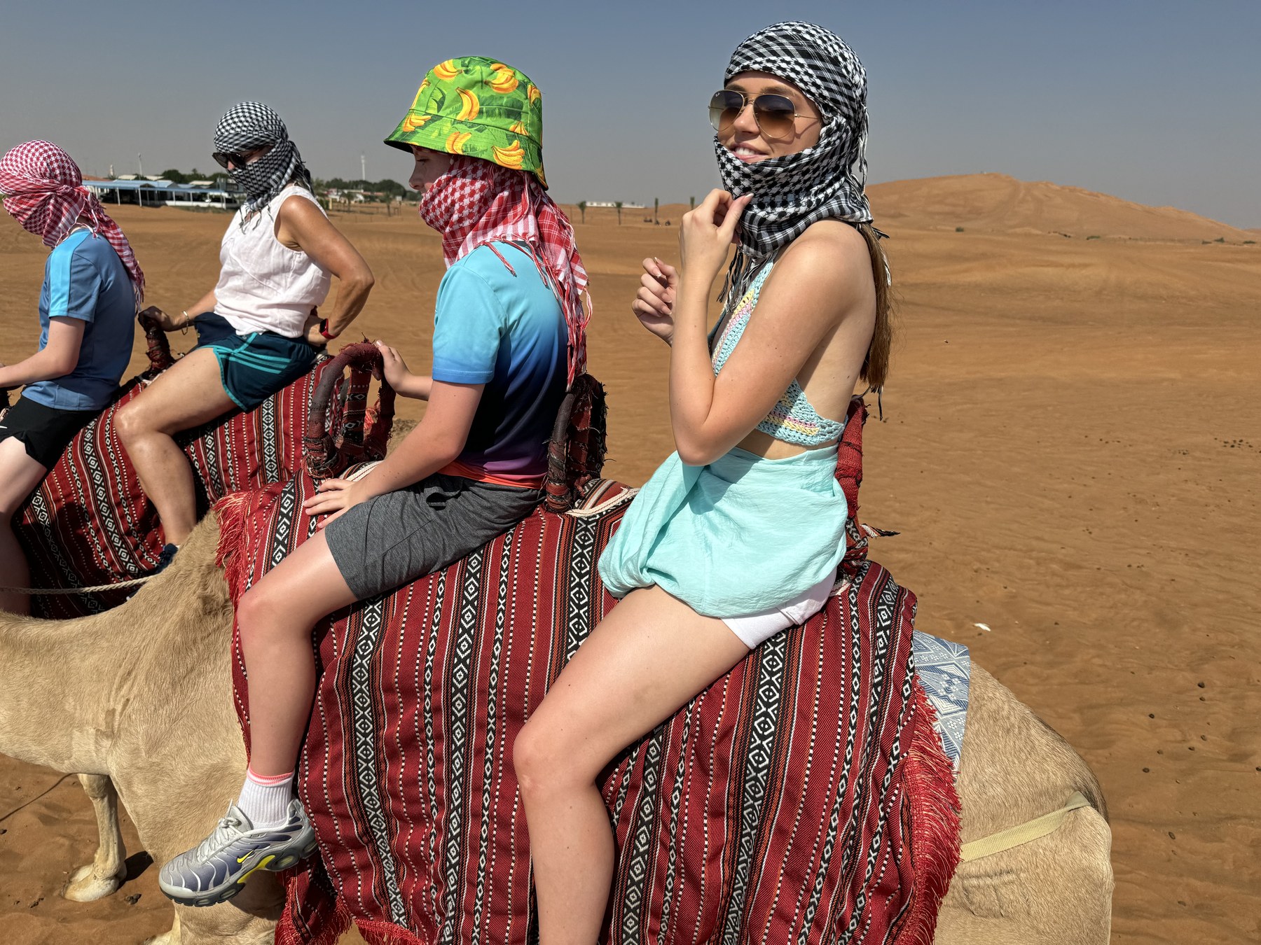A group on a camel ride in a sandy landscape under a clear sky.